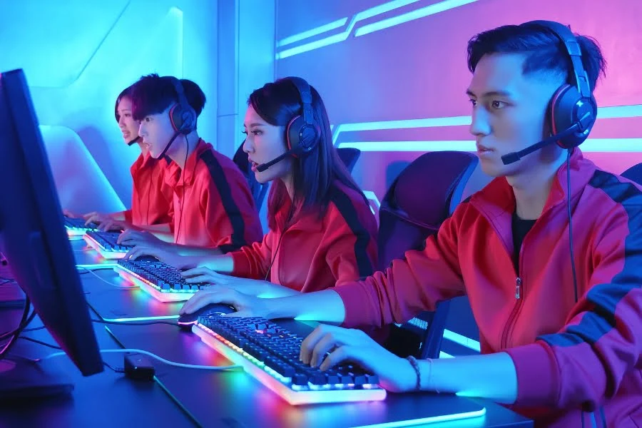 E-Sport: Wie Gaming zum professionellen Sport wurde 2 E-Sport-Team mit Headsets spielt gemeinsam an Gaming-PCs in einem blau und pink beleuchteten Raum