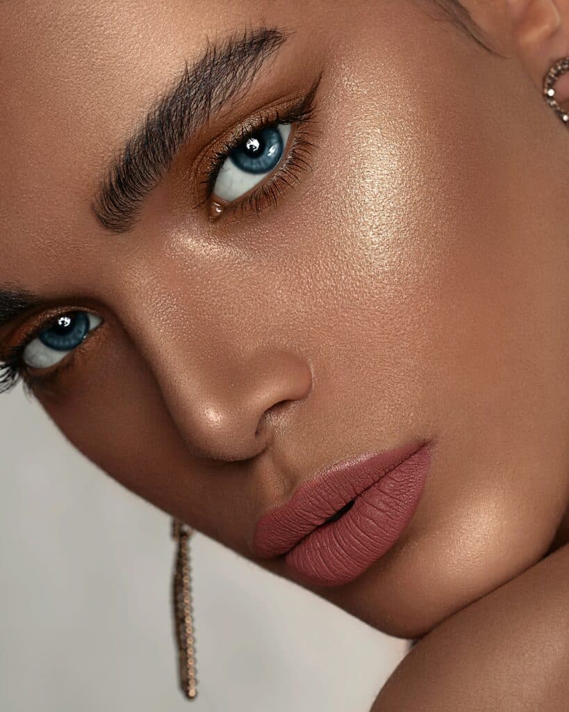 Model mit starkem Bronzer, glänzendem Gesicht, Mattem Lippenstift, blaue Augen. Der klassische Sommerglow.
