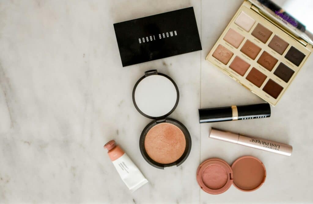 Make-up sortiert auf Marmortisch. Produkte von Bobbi Brown, Lidschatten farblich braun, bronzing Puder, Lippenstift und Concealer.