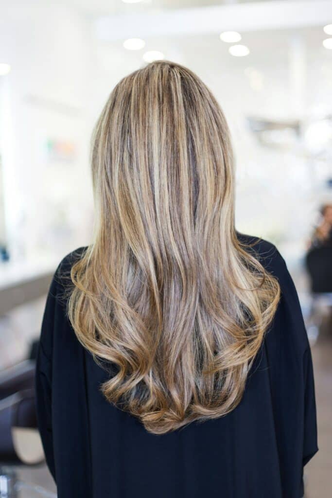 Frau die ihre Haare von hinten zeigt. Frisch aus dem Frisur, hat sie blone Haare mit Wellen. 