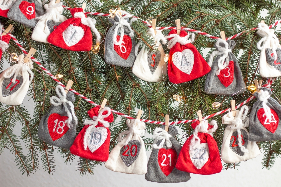 kleine Säckchen an einer Girlande in rot, grau, weiß, Tannenzweige im Hintergrund