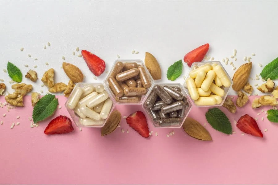 Supplements im Check: Was sie wirklich können und für wen sie sich lohnen! 2 Hintergrund rosa weiß, Vordergrund verschiedenen Pillen, Blätter, Früchte, Nüsse