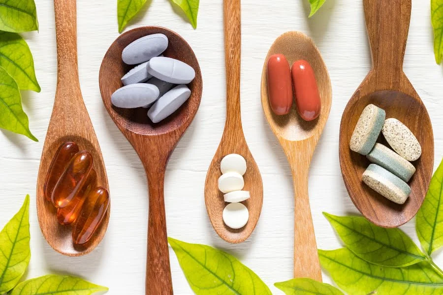 Supplements im Check: Was sie wirklich können und für wen sie sich lohnen! 5 bunte Supplements auf Löffeln aus Holz, Blätter im Hintergrund.