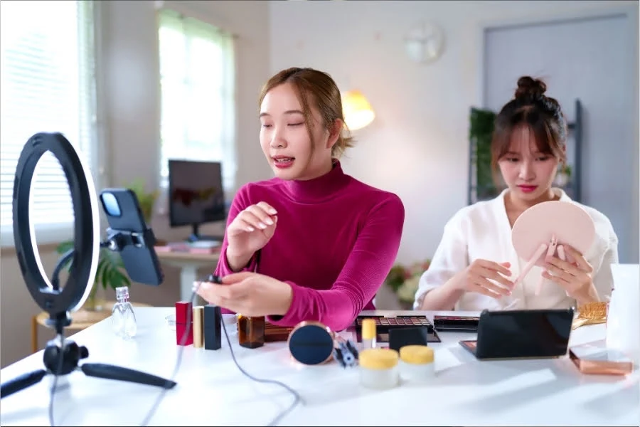 Zwei Frauen nehmen Kosmetikprodukte an einem Tisch auf und präsentieren Make-up vor einer Kamera mit Ringlicht