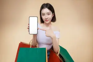 Frau hält Smartphone mit leerem Bildschirm und zeigt darauf während sie mehrere Einkaufstaschen trägt