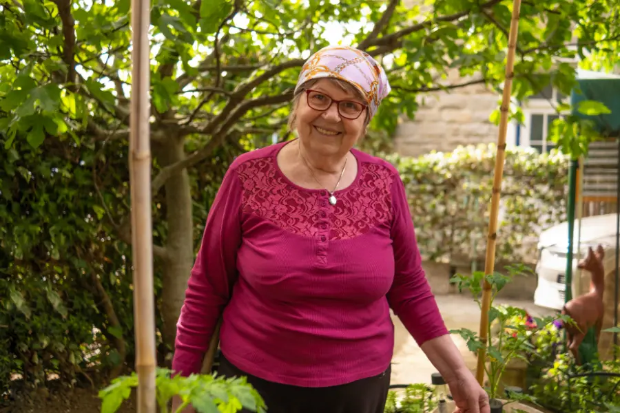 Balkon oder Garten – So gestaltet ihr euer privates Paradies 4 Fröhliche ältere Frau steht im Garten zwischen Gemüsepflanzen und lächelt in die Kamera.