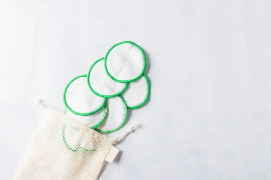 Zero Waste im Alltag - 5 einfache Tipps für's Badezimmer 13 Mehrere wiederverwendbare Abschminkpads aus Stoff mit grünem Rand liegen neben einem Stoffbeutel auf hellem Untergrund. Die nachhaltigen Kosmetikpads dienen zur umweltfreundlichen Gesichtsreinigung.